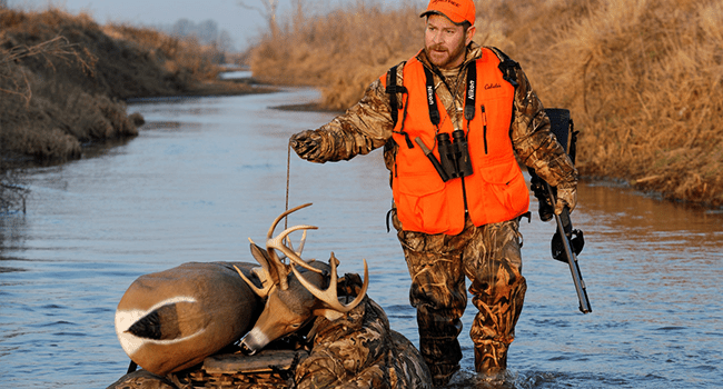 Male hunter wearing blaze orange floating a decoy down a shallow creek