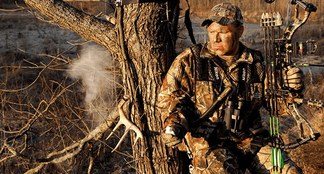Male bow hunter in a tree stand watching wind